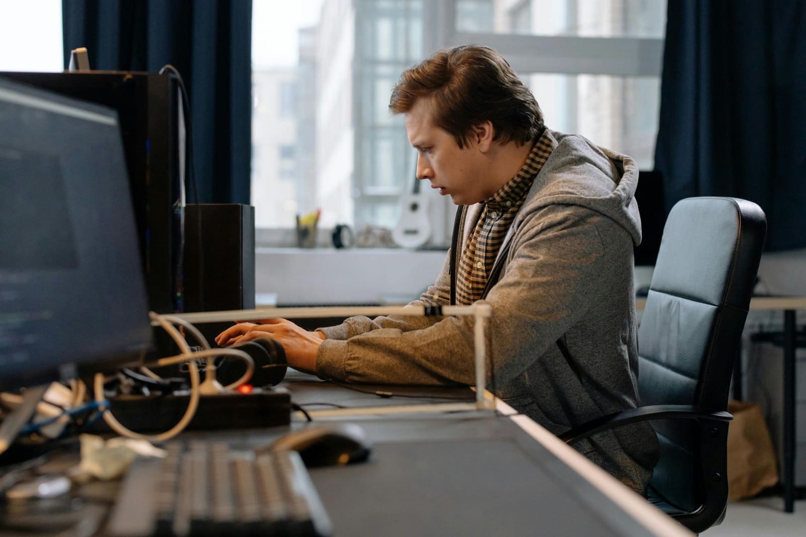 Man in a grey hoodie sitting at a table working on a laptop