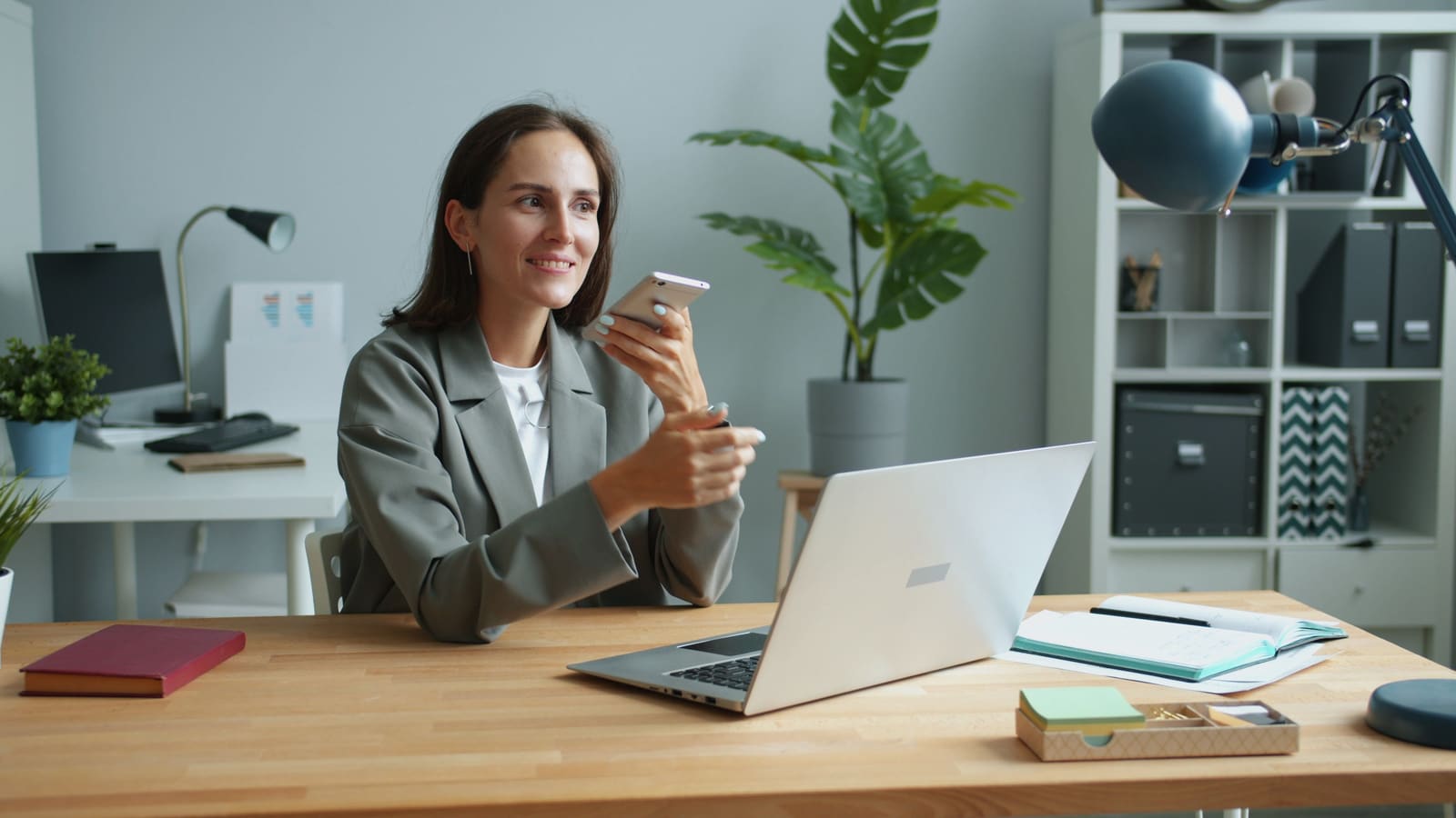 A businesswoman using a smartphone and laptop together at her desk