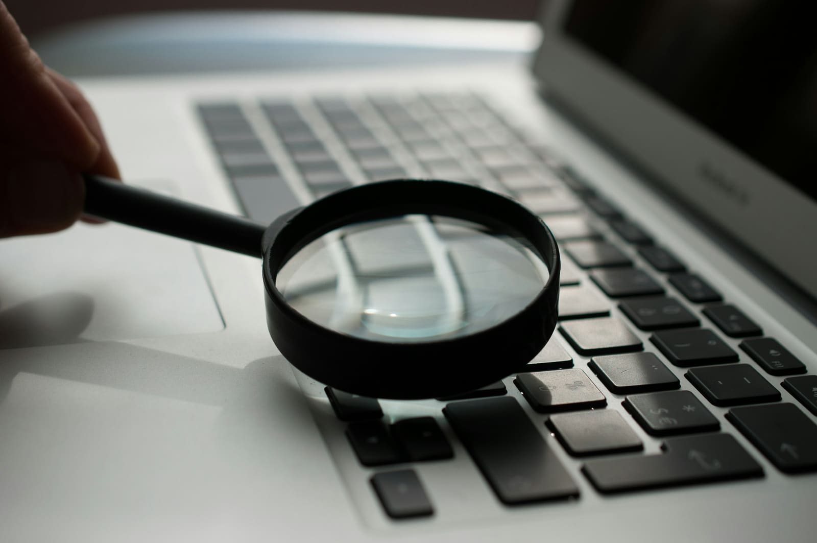 A magnifying glass resting on a desk next to a laptop